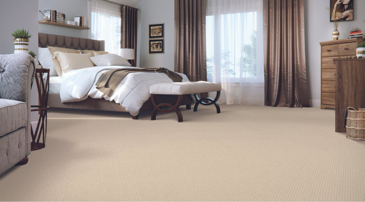 Bedroom scene with beige cut carpet, white bed with bronze color theme in room, wooden decor